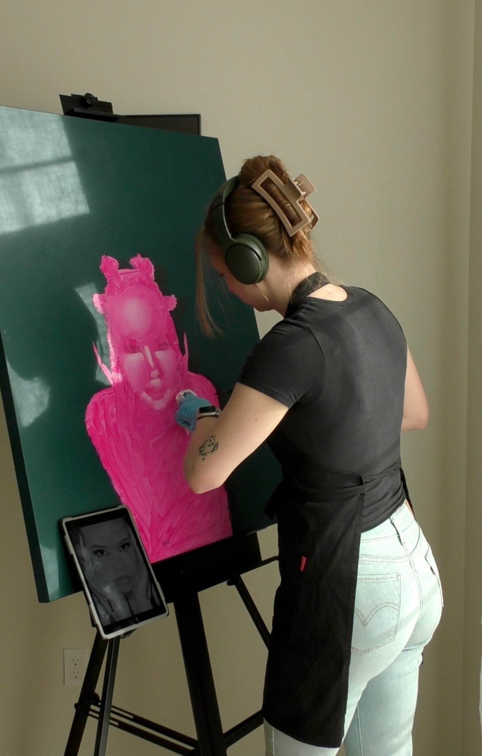 Person wearing headphones and working on a magenta underpainting with a tablet being used for a reference photo.