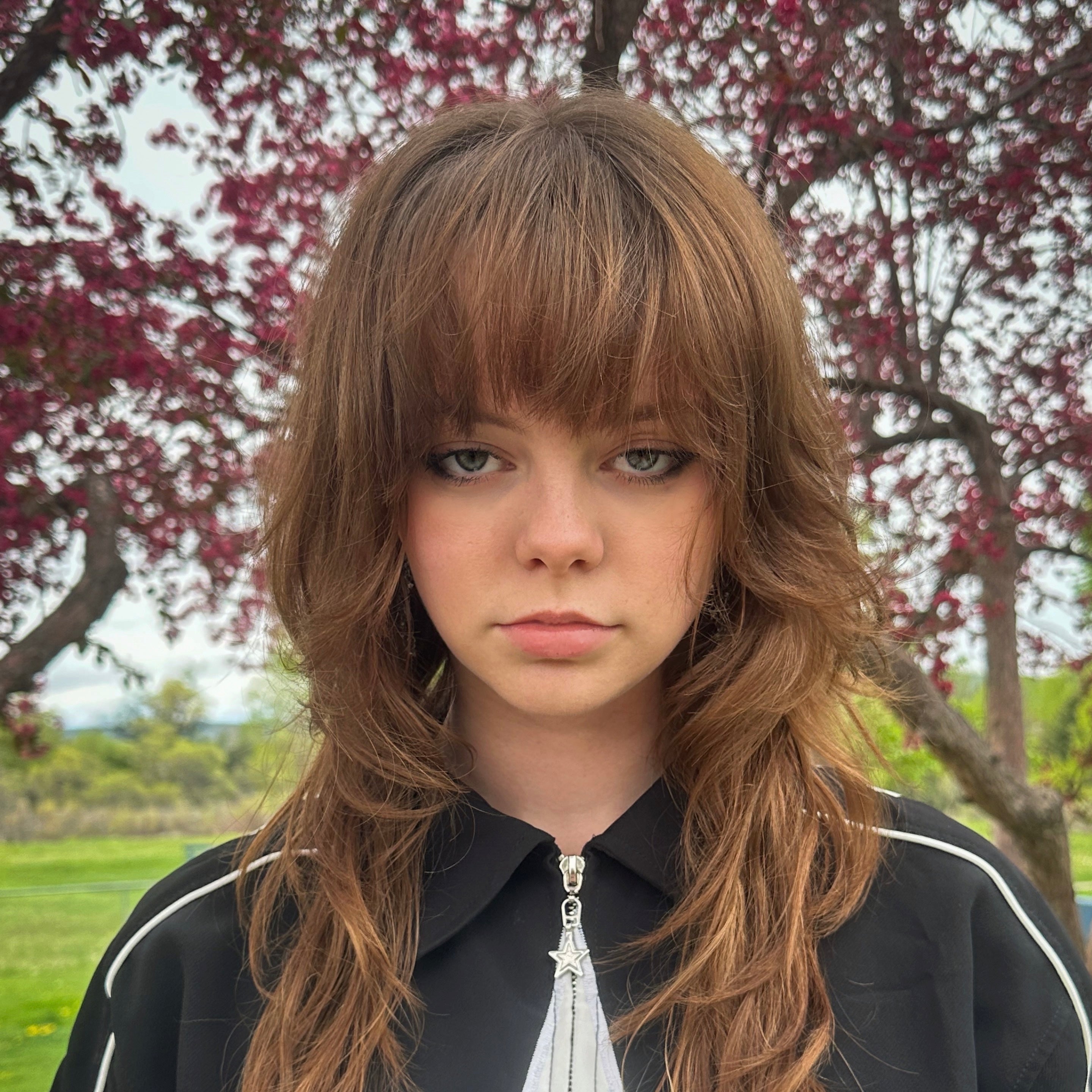Person with long brown hair standing outdoors with trees in the background