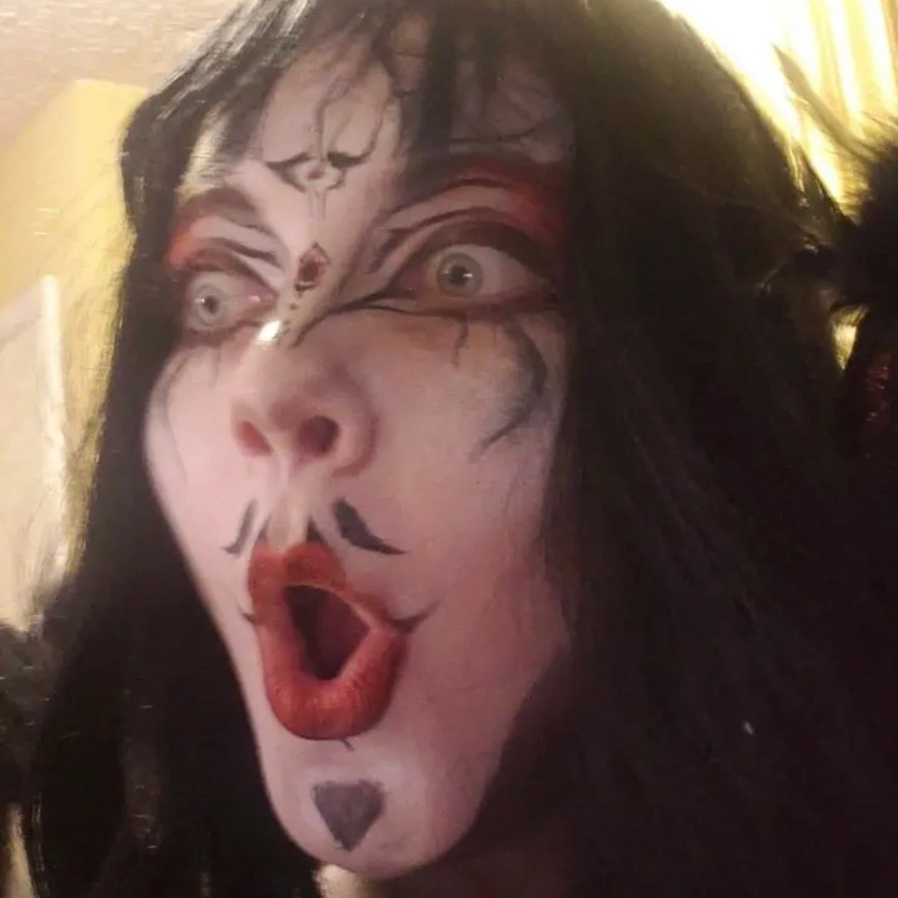 Person with dramatic makeup, including red lipstick and black eye makeup, against a neutral background.