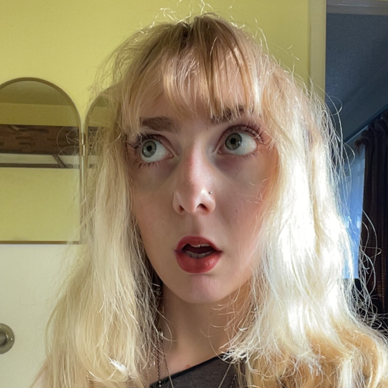 Person with long blonde hair and a surprised expression indoors.