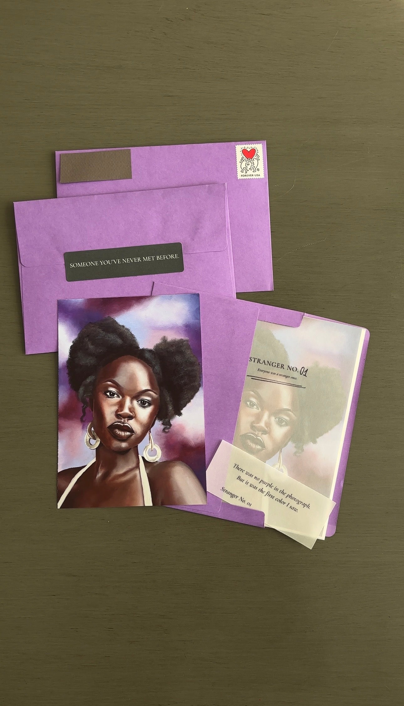 Purple evelopes and art print with a woman's face and a smaller card on a brown background