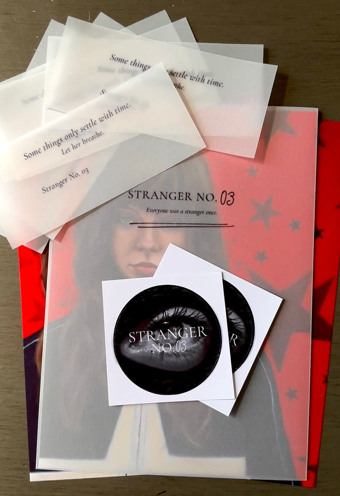 Collection of 'Stranger No.03' themed items including ephemera cards and stickers on a wooden surface.