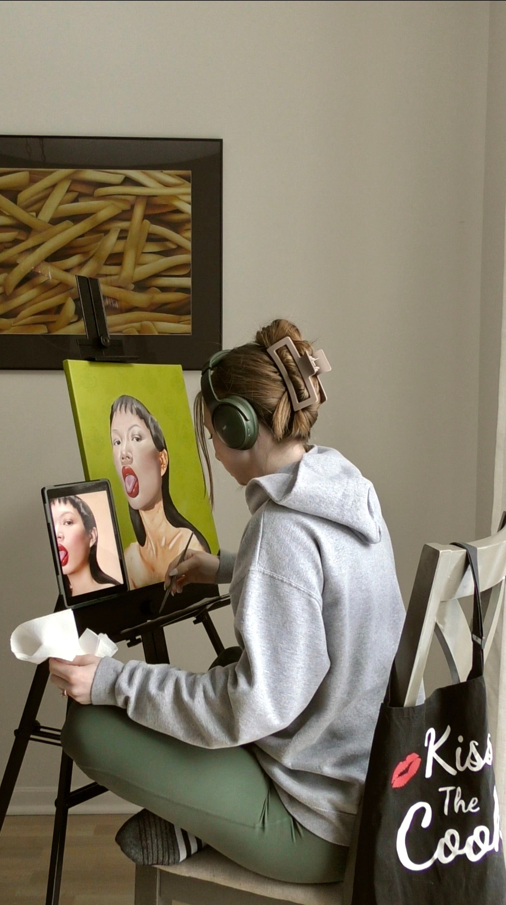 Person sitting on a chair with headphones on, painting a portrait of a woman's face for the 2026 birthday print.